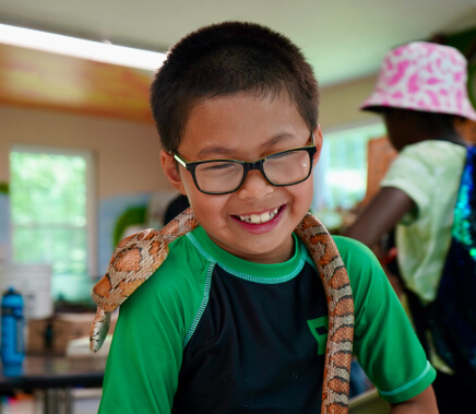 Kid smiles with a snake on his shoulder in College Settlement Camps in Horsham, PA