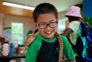 Kid smiling with an orange snake wrapped over his shoulders